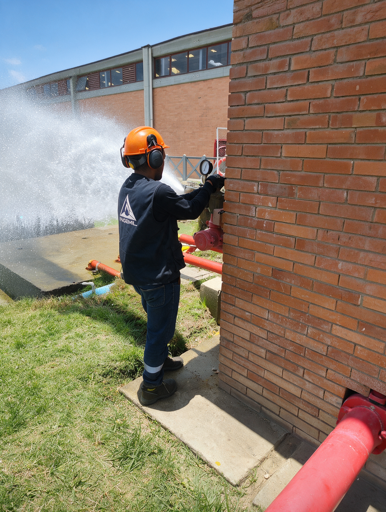 Técnico de INGEMIL realizando prueba de hidrante con chorro de agua junto a un muro